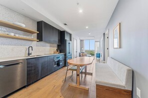 A modern kitchen with a dining area, wooden flooring, and a view to the outside. - Luxury 1BR Natiivo Condo with Lake View and Rooftop Heated Pool near Rainey St (Austin)