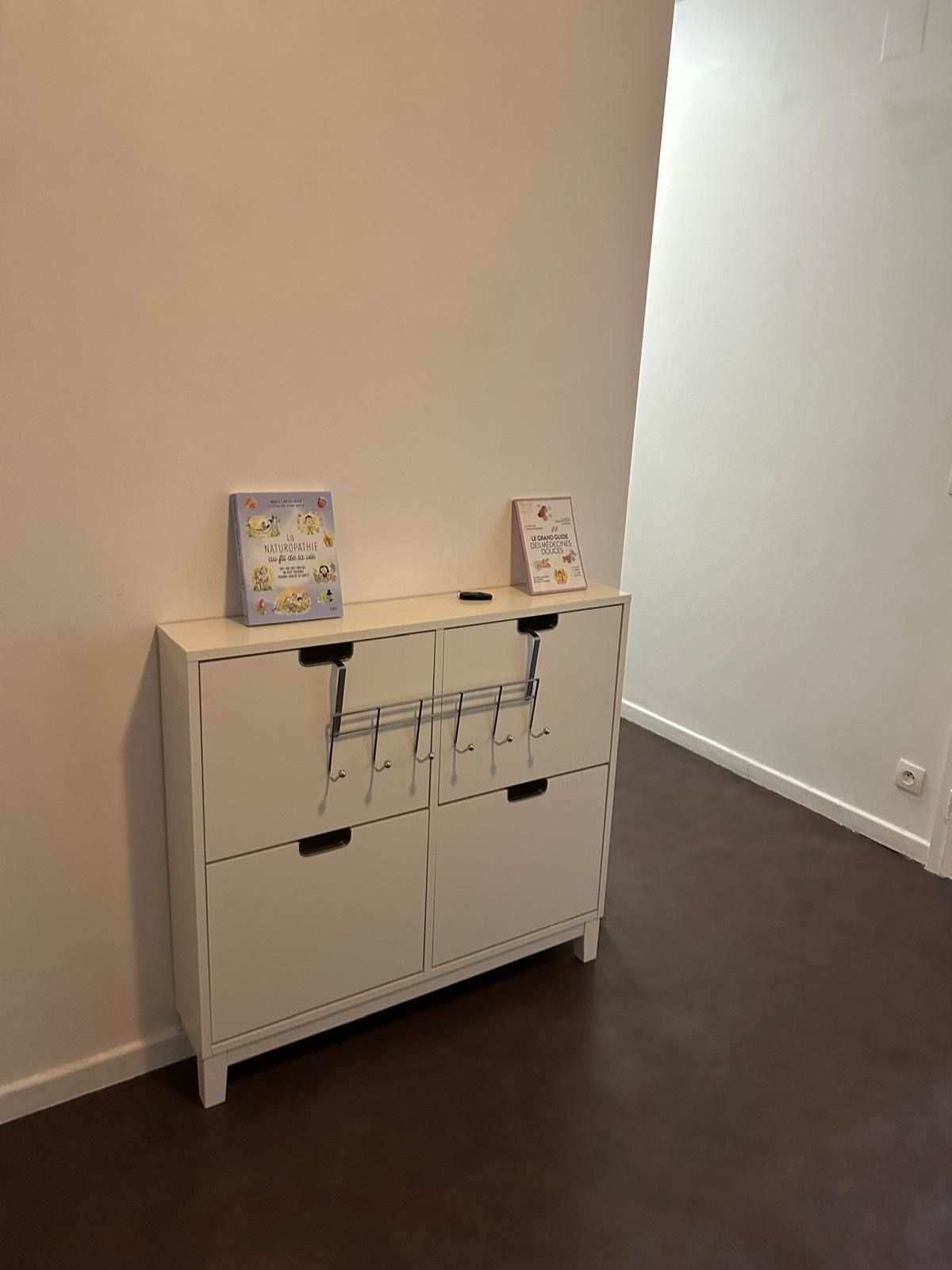 A white cabinet with two drawers and a shelf, against a plain wall.