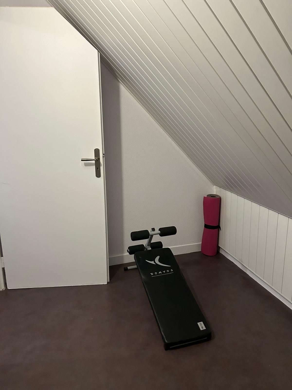 A small room with a white door, a black exercise bench, and a pink yoga mat.