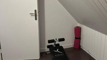 A small room with a white door, a black exercise bench, and a pink yoga mat.