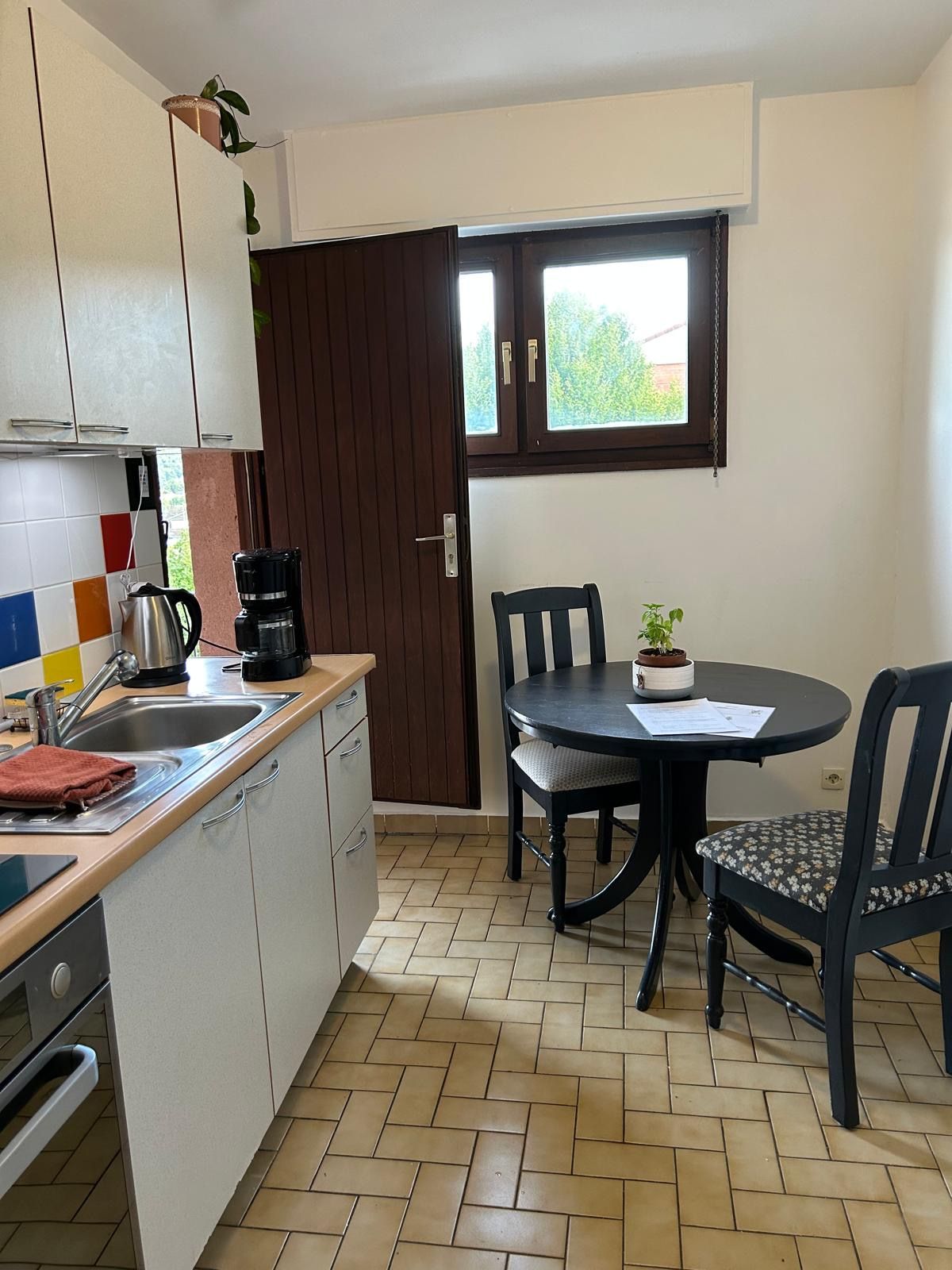 A compact kitchen with a dining area, a window with a view, and a small potted plant on the table.