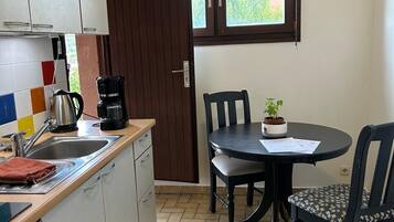 A compact kitchen with a dining area, a window with a view, and a small potted plant on the table.