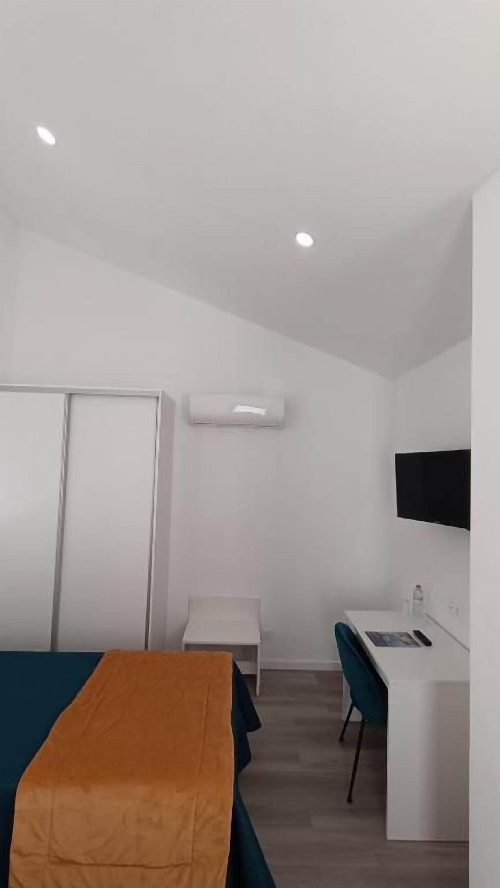 A hotel room with a bed, a desk, a chair, a wardrobe, and an air conditioning unit.