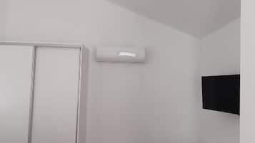 A hotel room with a bed, a desk, a chair, a wardrobe, and an air conditioning unit.
