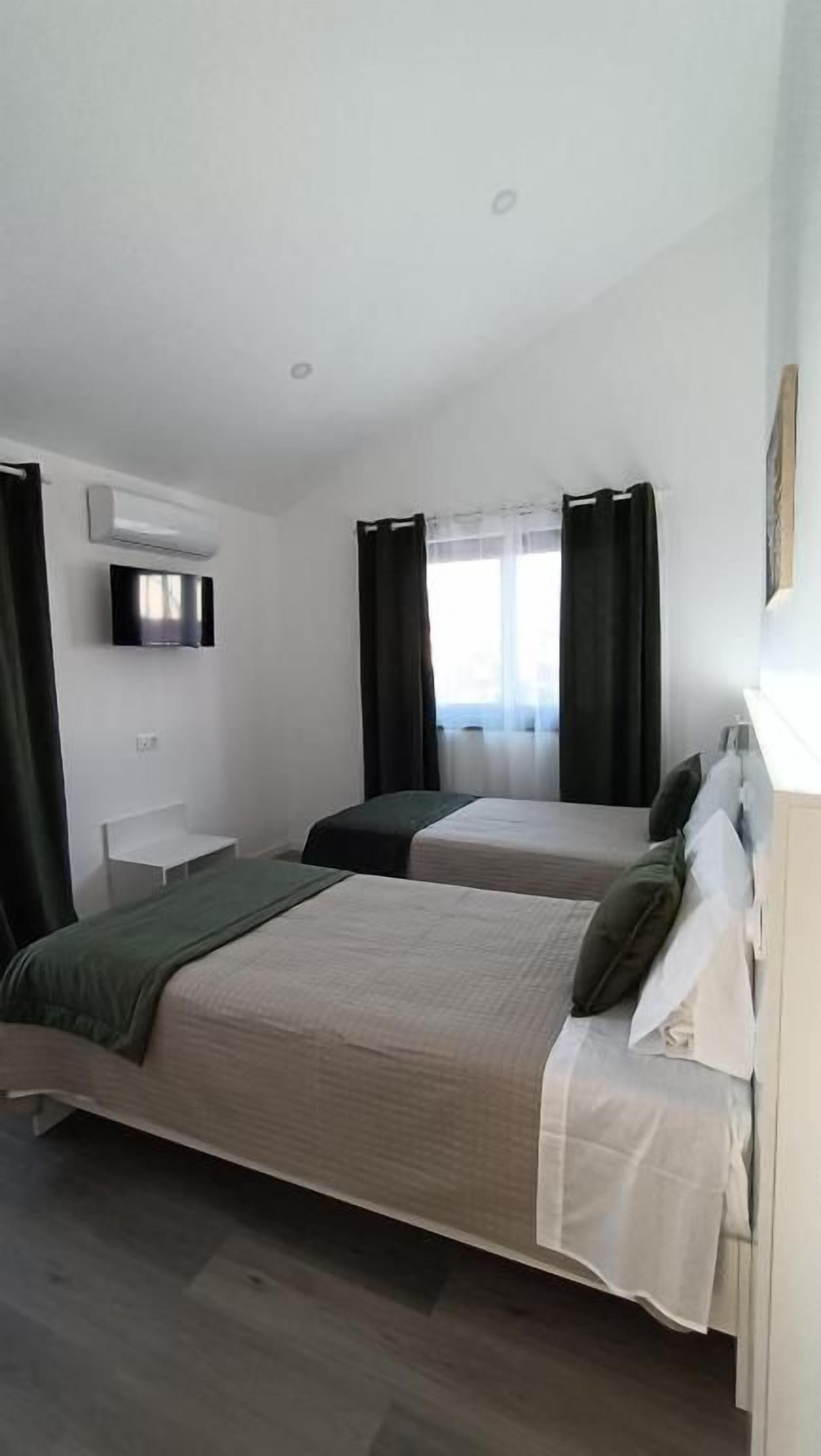 Et hotelværelse med to senge, et fladskærms TV, et skrivebord og et vindue med gardiner.