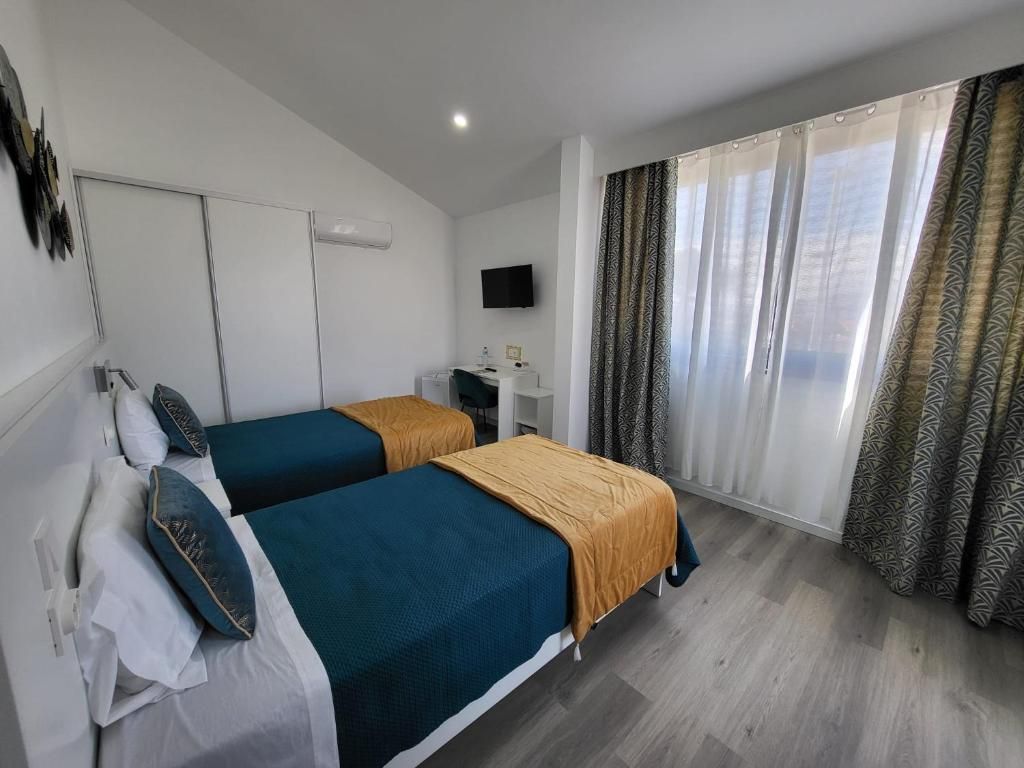 A hotel room with two beds, a desk, a television, and a large window with curtains.