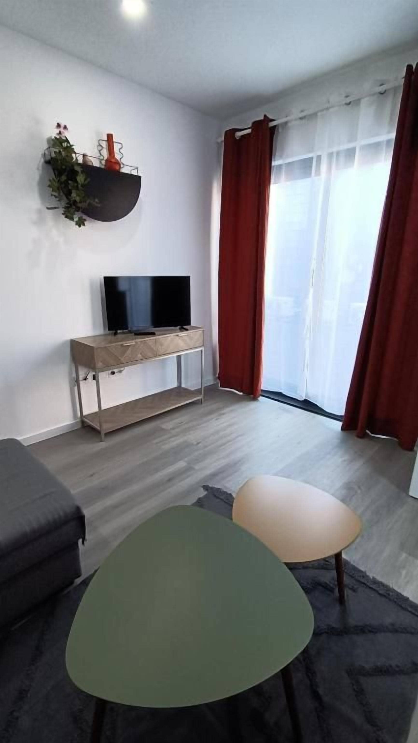 A modern living room with a flat-screen TV on a wooden console, a sofa, and two ottomans.