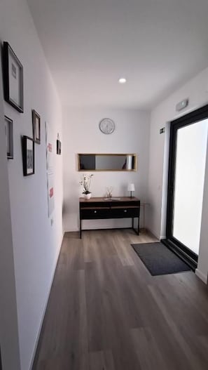 A hallway with a wooden floor, a black console table with a mirror, framed pictures on the wall, and a door leading to another room.