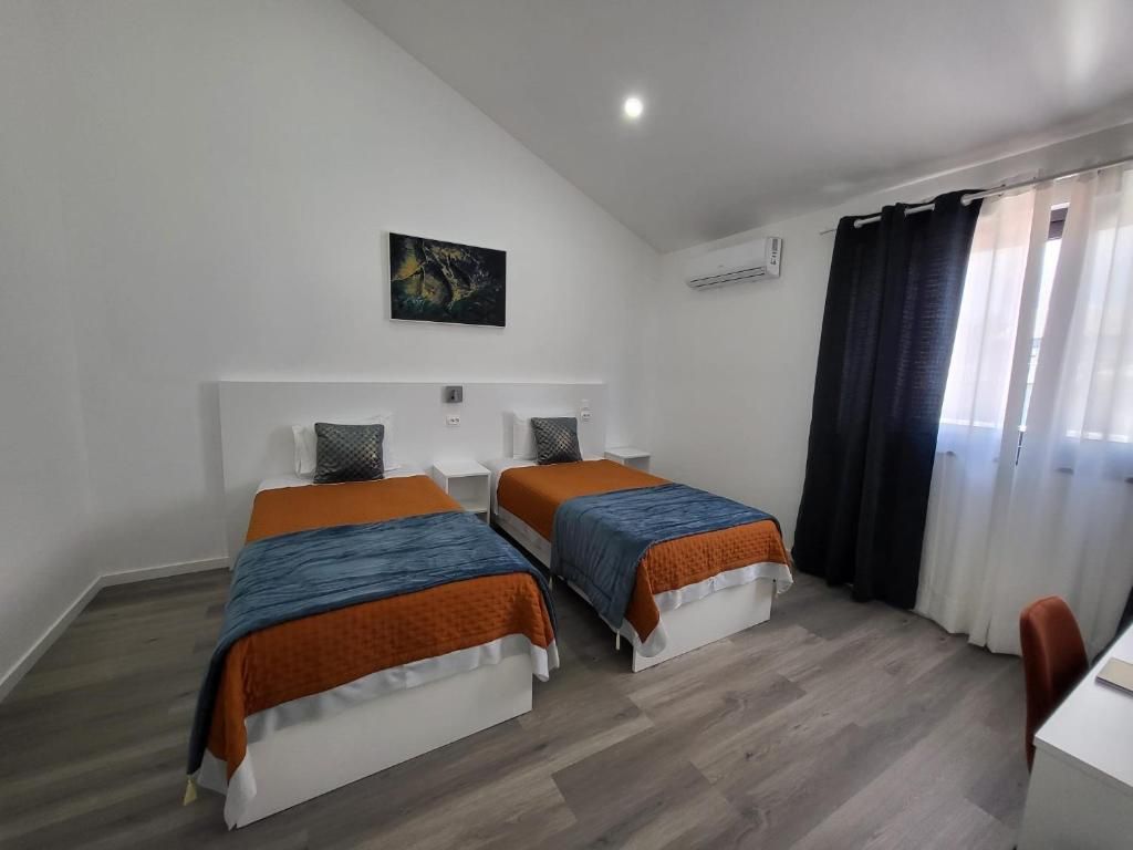 Habitación de hotel con dos camas, un escritorio, una silla, un cuadro en la pared y una ventana con cortinas.