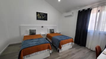 Habitación de hotel con dos camas, un escritorio, una silla, un cuadro en la pared y una ventana con cortinas.