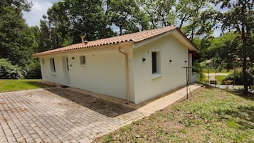 A small, single-story building with a tiled roof, a paved entrance, and a grassy area with trees.
