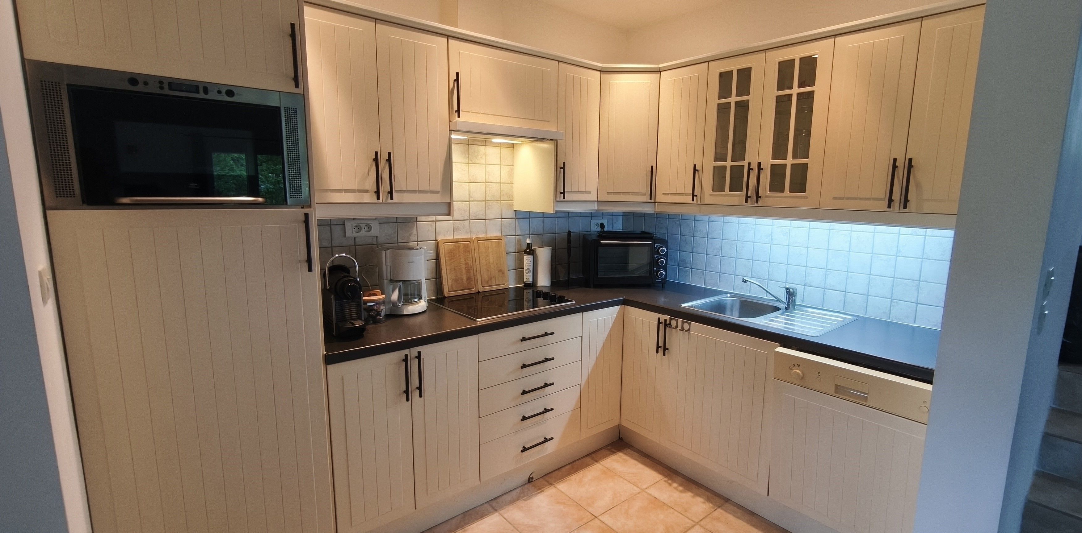 A compact kitchen with white cabinets, a microwave, a coffee maker, a toaster, and a sink.