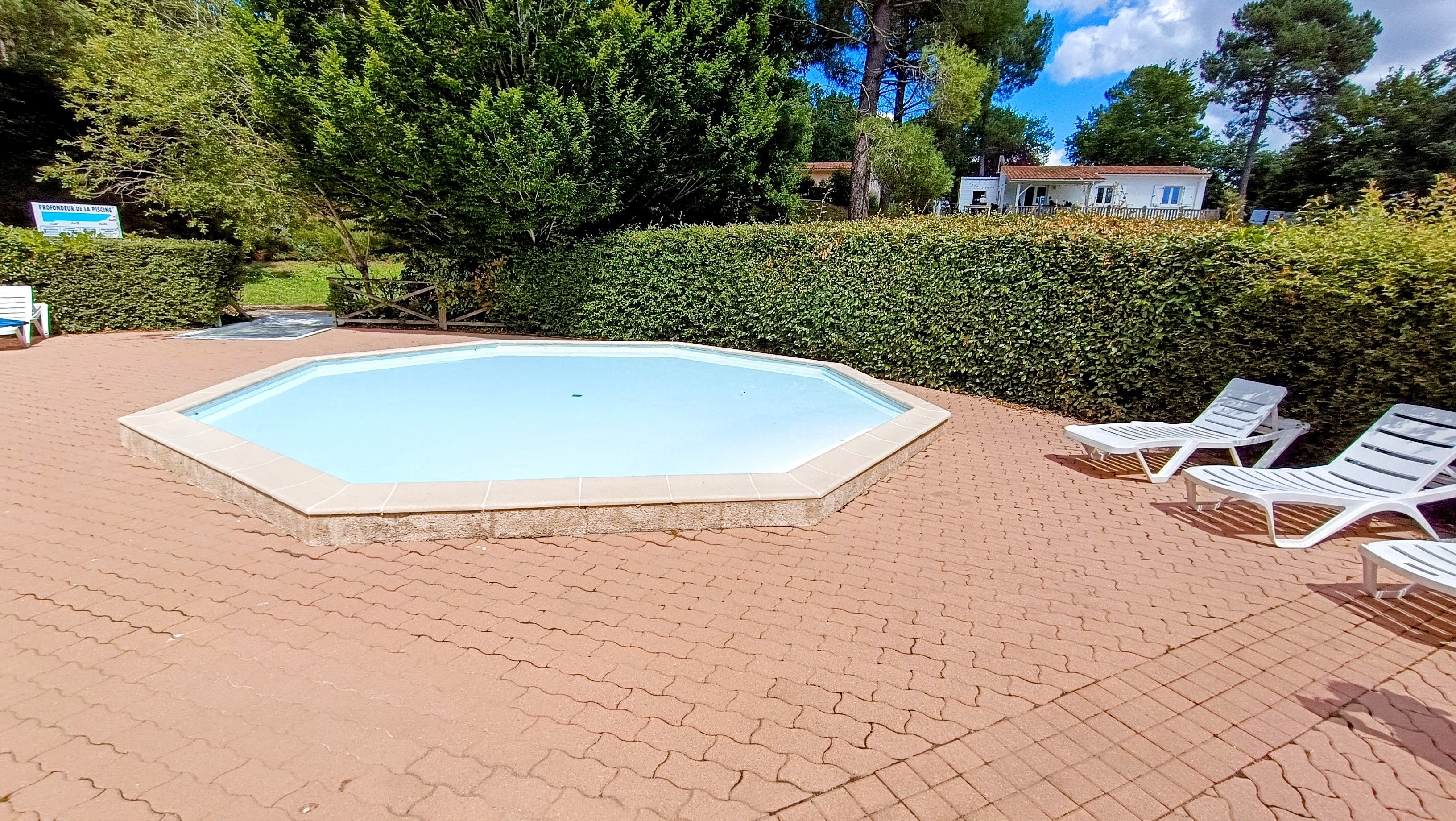 Une piscine rectangulaire dont le bord est recouvert de carrelage, entourée d’une zone pavée avec des chaises longues blanches.