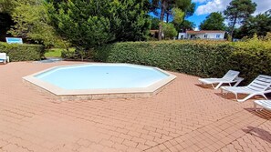 Une piscine rectangulaire dont le bord est recouvert de carrelage, entourée d’une zone pavée avec des chaises longues blanches.