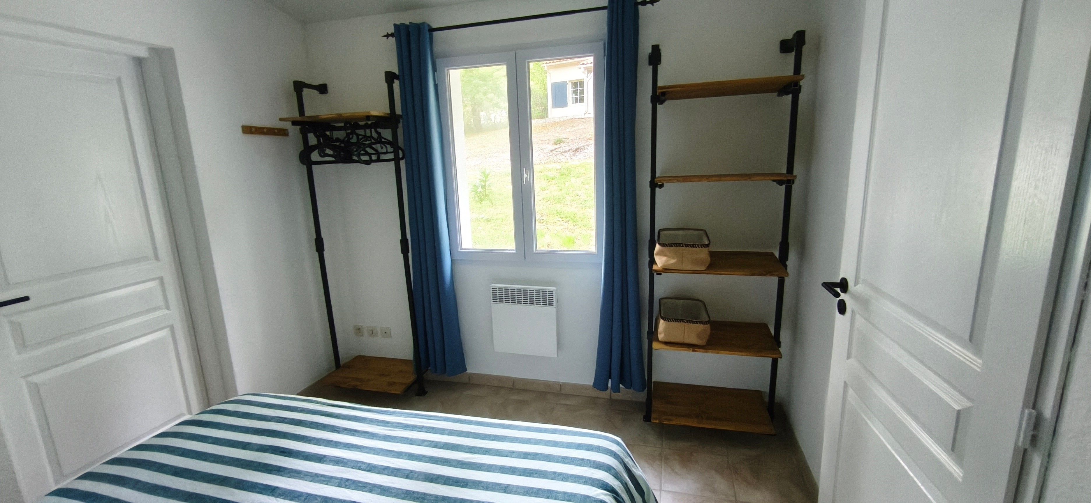 Een kamer met een bed, een raam met gordijnen, een radiator en planken met opbergdozen.