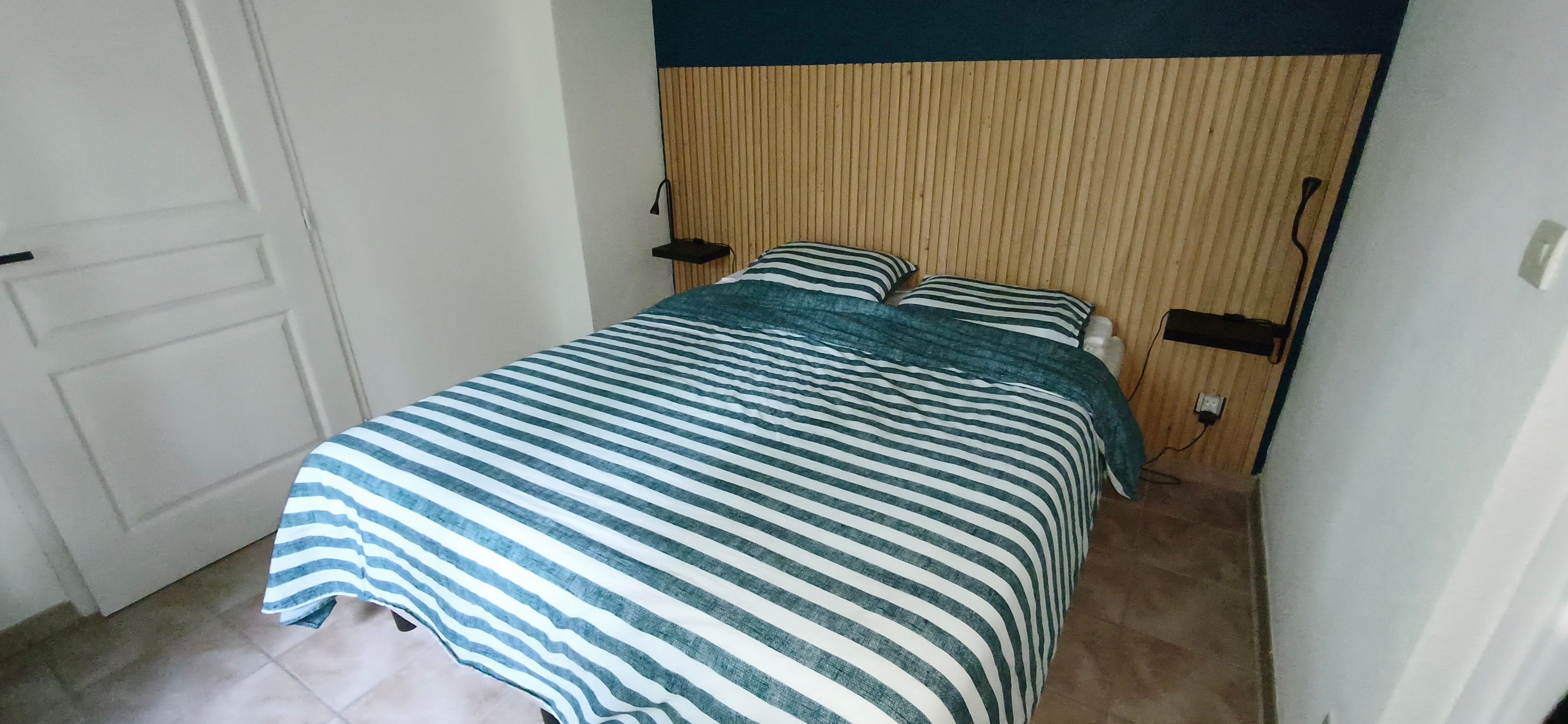 A small, neatly made bed with a striped bedspread, a wooden headboard, and two bedside lamps.
