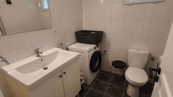 Ein kleines Badezimmer mit Waschbecken, Waschmaschine, Toilette und Spiegel.