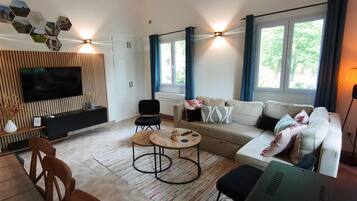 Een moderne woonkamer met een flatscreen televisie, een zithoek, een salontafel en een eethoek met stoelen.