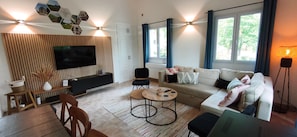 Una sala de estar moderna con un televisor de pantalla plana, un conjunto de sofás, una mesa de centro y un comedor con sillas.