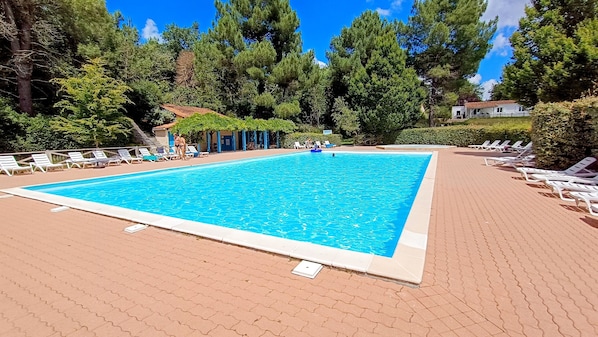 Una piscina rectangular con borde de azulejos, rodeada de sillas de descanso y una terraza pavimentada.