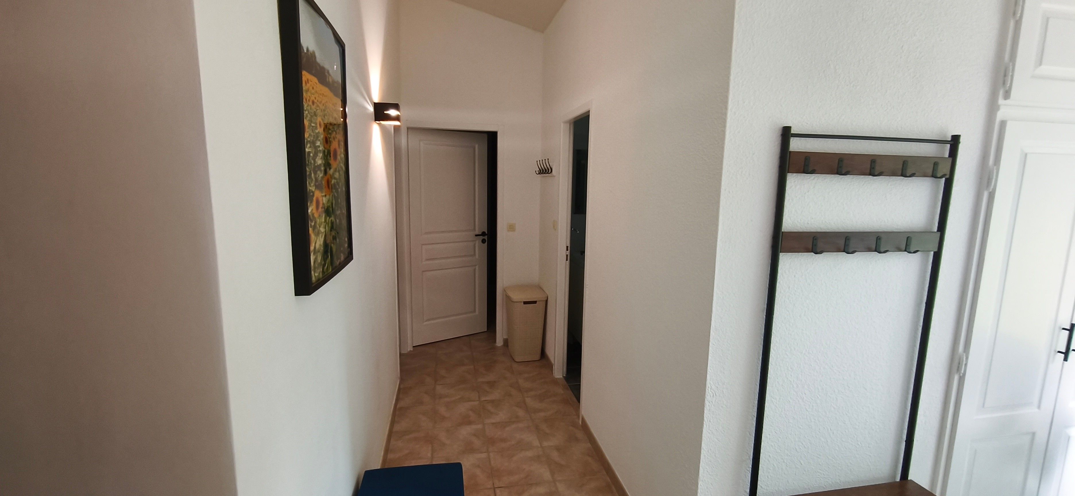 A narrow hallway with a door at the end, a trash bin, and a coat rack.