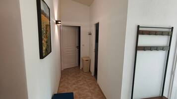 A narrow hallway with a door at the end, a trash bin, and a coat rack.