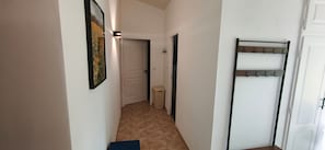 Passadís estret amb una porta al final, un safata d'escombraries i una perxa per a abrics.