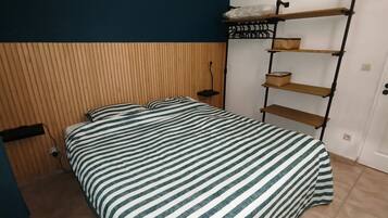 Een slaapkamer met een bed, nachtkastje, een wandplank en een deur.