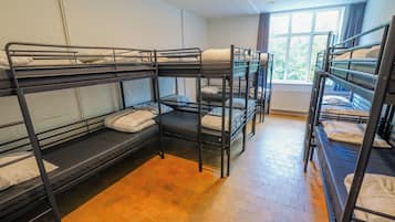 Een slaapzaal met stapelbedden, een raam met gordijnen en een radiator.