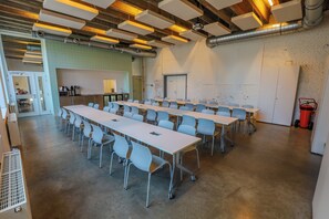Una sala conferenze con diversi tavoli e sedie, un angolo cottura e un muro in mattoni.