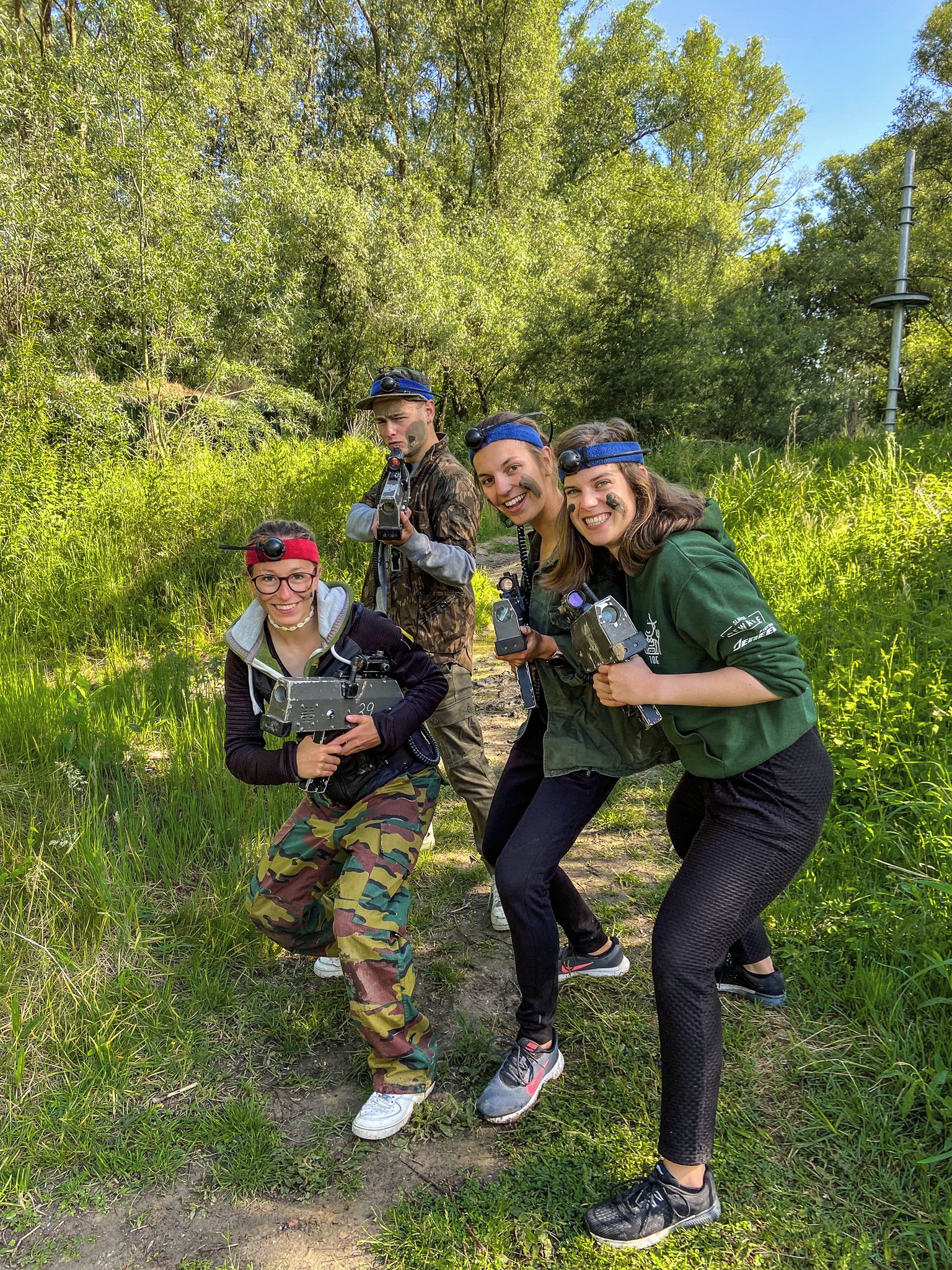 En gruppe mennesker i et udendørs miljø med træer og grøn vegetation i baggrunden.