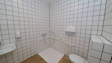 Een badkamer met witte betegelde wanden, een wit wastafelmeubel, een toilet en een douche met een handgreep.