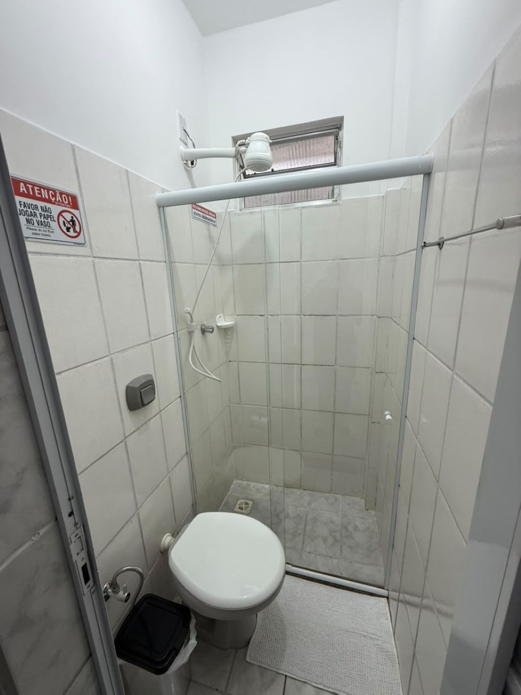 Een kleine, afgesloten douchecel met een toilet en een prullenbak.