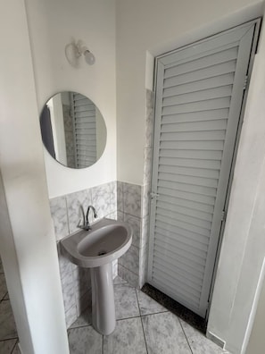 Casa de banho com lavatório sobre pedestal, espelho redondo e porta fechada.