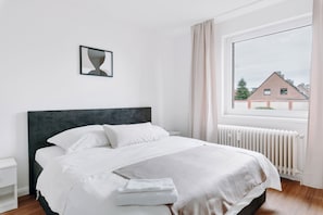 Et soveværelse med seng, et natbord, et vindue med gardiner og en radiator.