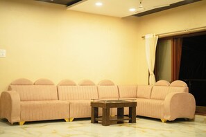 A living room with a sofa set, a coffee table, and a window with curtains. - Spacious 8-bedroom hotel in welcoming Kashid with AC comfort. (Kashid, Alibaug)