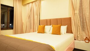 Quarto de hotel com uma cama grande, cortinas bege e janela com vista.