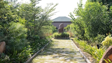 A pathway leading to a building with a tiled roof, surrounded by lush greenery and a stone border.