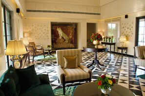 Um hall de hotel com piso quadriculado, um mural grande de tigre e uma área de estar com sofá e poltronas.