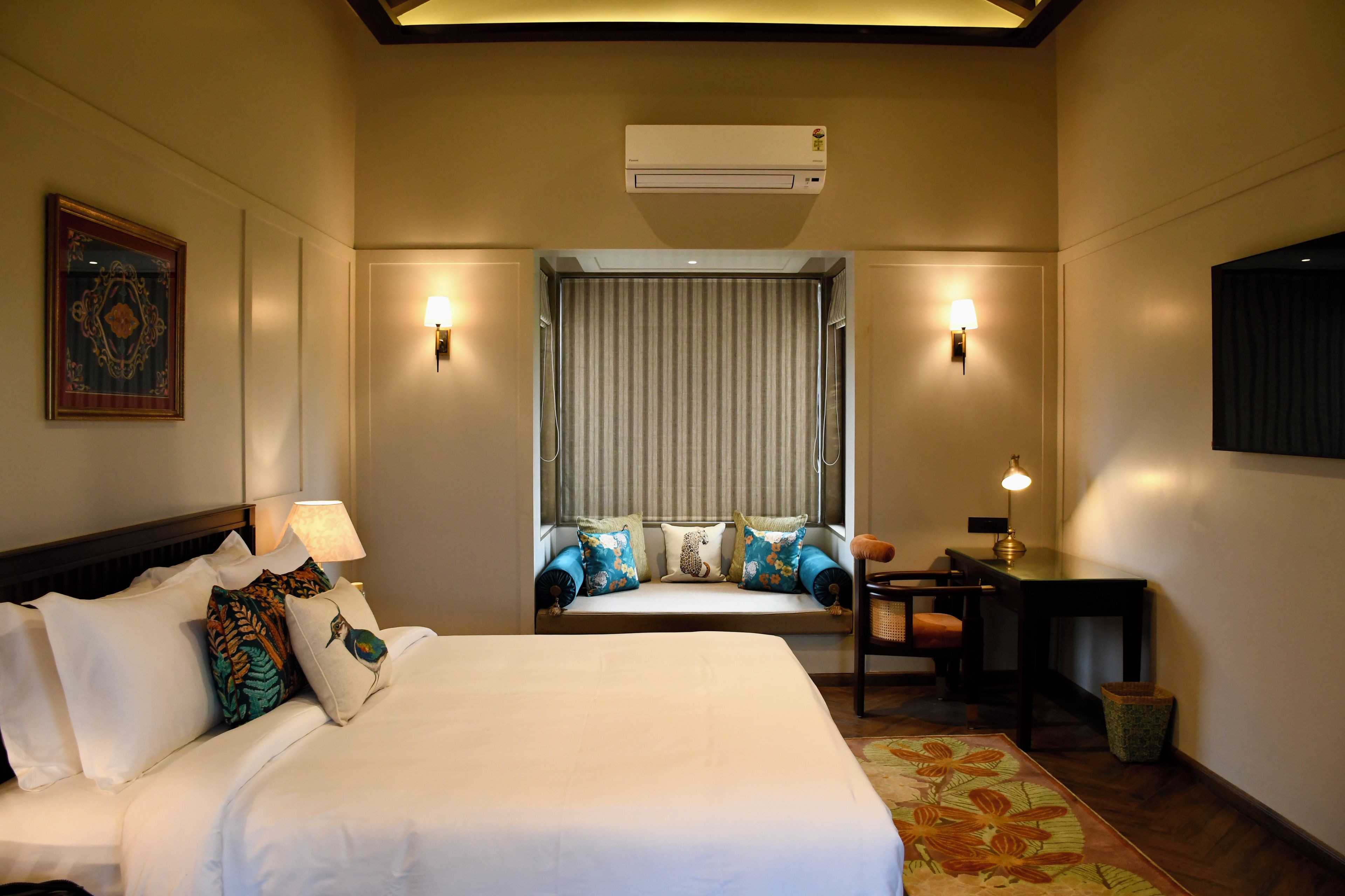 Een hotelkamer met een bed, een bureau, een stoel, een lamp, een raam met gordijnen en een airconditioning.