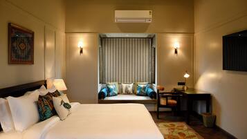 Een hotelkamer met een bed, een bureau, een stoel, een lamp, een raam met gordijnen en een airconditioning.