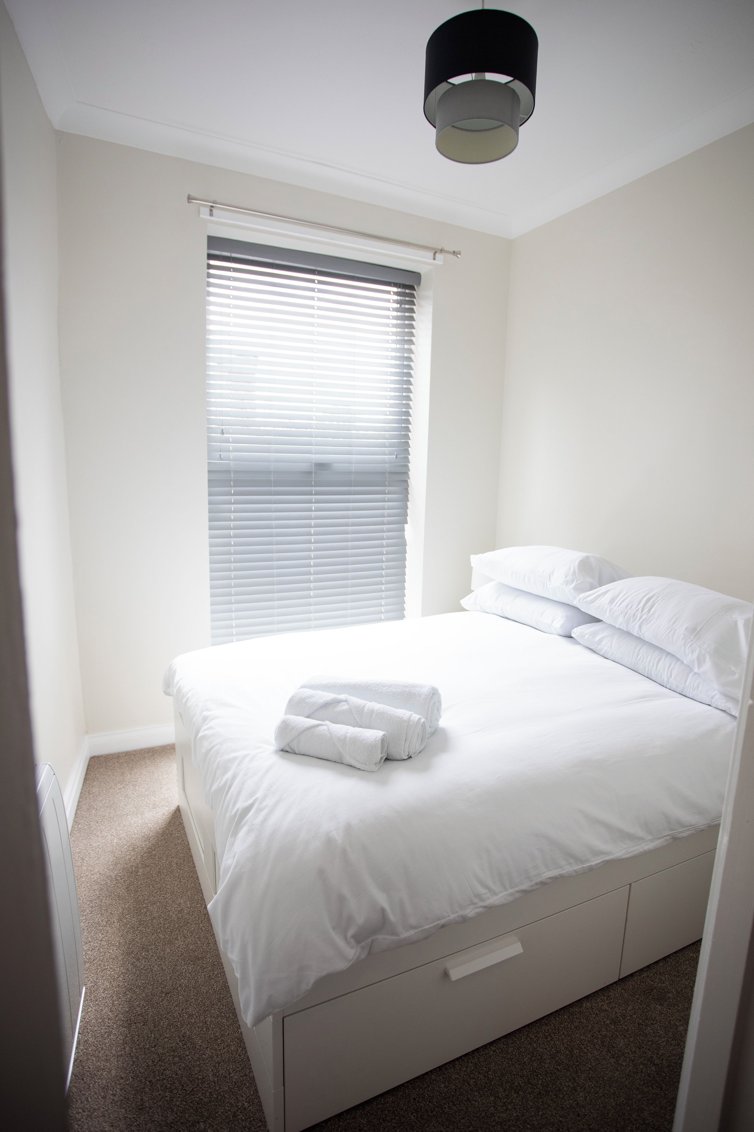 Ein Schlafzimmer mit einem Bett, einem Fenster mit Jalousien und einer Deckenleuchte.