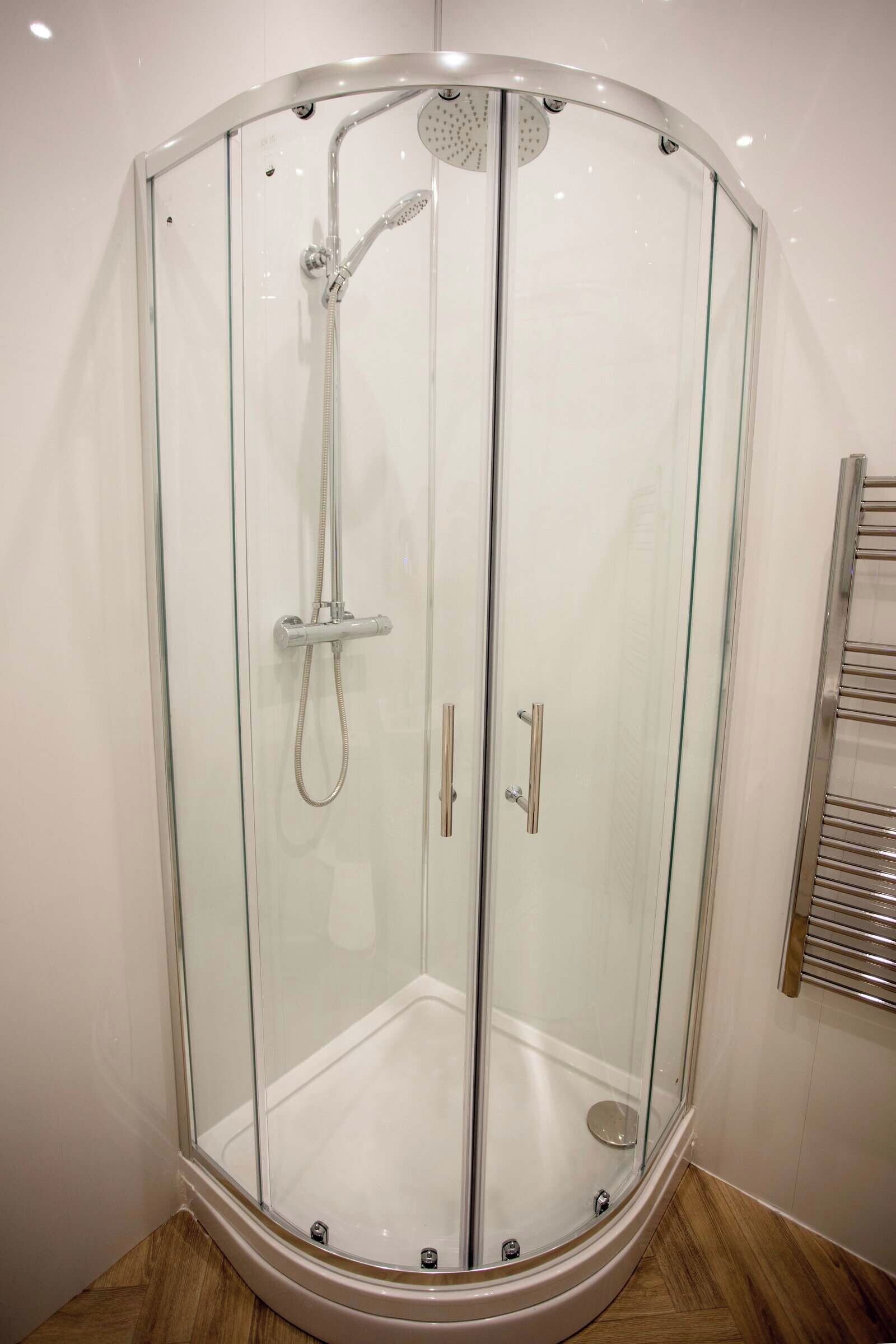 A glass-enclosed shower stall with a handheld showerhead and a wall-mounted faucet.