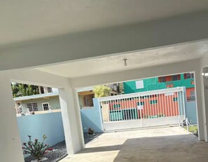 A covered outdoor area with a gated entrance, a concrete floor, and a view of colorful buildings in the background. - Brisas Del Atlantico House (Luquillo)
