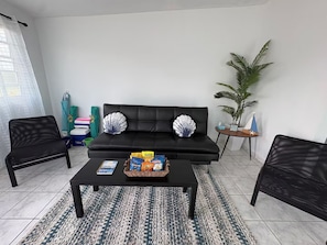 A living room with a black sofa, two armchairs, a coffee table with snacks, a potted plant, and a small table with a model sailboat. - Brisas Del Atlantico House (Luquillo)