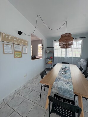 Een eethoek met een lange tafel, stoelen, een hanglamp en een wand met ingekaderde certificaten.