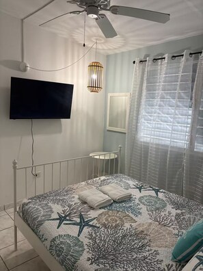A bedroom with a bed, a ceiling fan, a mounted TV, a bedside table, and a window with curtains. - Brisas Del Atlantico House (Luquillo)
