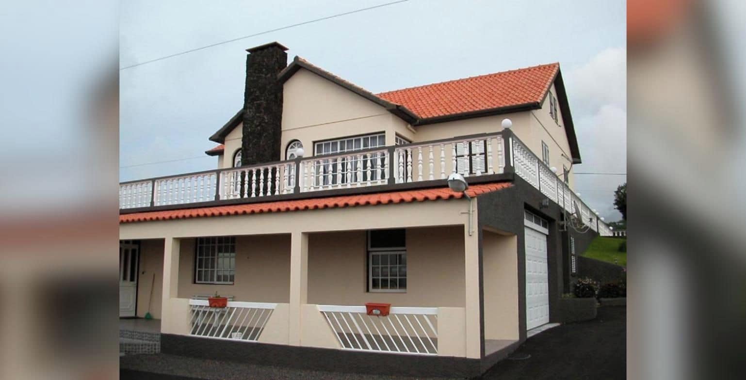 A two-story building with a balcony, a garage, and a chimney.