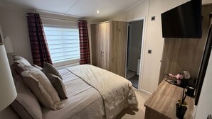 Ein Schlafzimmer mit Bett, Fernseher, Kleiderschrank und einer Badezimmertür.