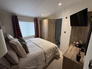 A bedroom with a bed, a TV, a wardrobe, and a bathroom door. - Cabin Sleeps 4 With Parking and Balcony (Chester)